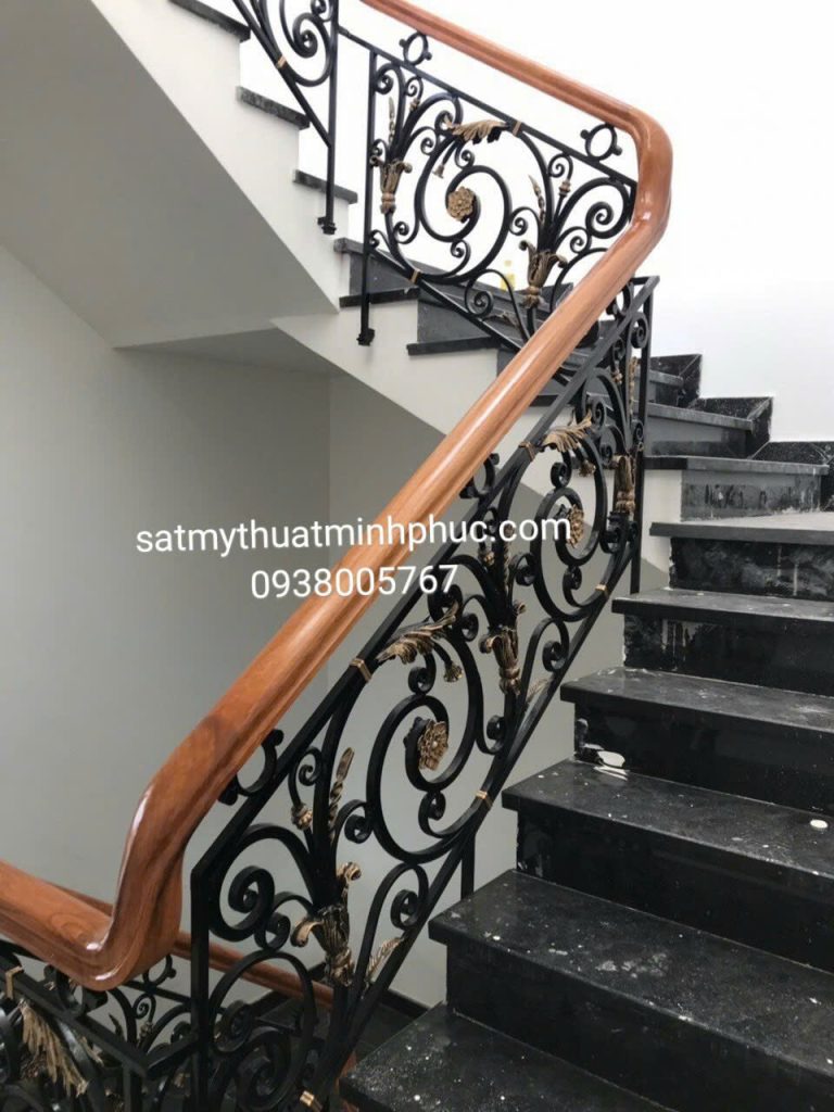 Lan can cầu thang sắt mỹ thuật Minh Phúc kết hợp hoa lá mạ vàng trên nền khung sắt đen, tay vịn gỗ liền mạch, bậc đá hoa cương màu đen.