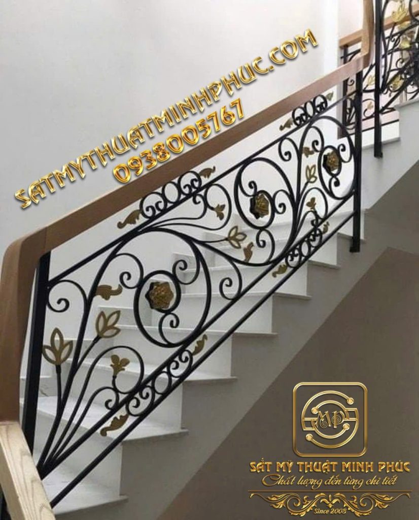 Lan can cầu thang sắt mỹ thuật Minh Phúc màu đen-đồng với hoa văn uốn lượn và tay vịn gỗ, lắp đặt dọc theo bậc thềm trắng.